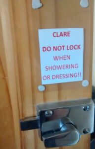A white notice with red text readin "Clare Do Not Lock When Showering Or Dressing"