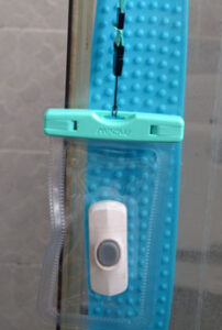 A doorbell in a waterproof smartphone bag, hanging from the doorhandle of a shower cubicle