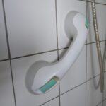 A white grab handle attched to bathroom tiles