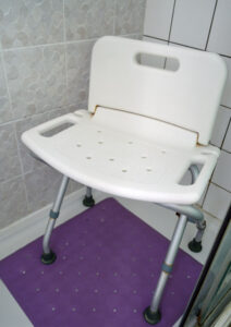A white shower seat sits in a shower cubicle with a purple mat underneath